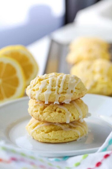 Three cake mix lemon cookies are stacked on top of each other on a white plate.