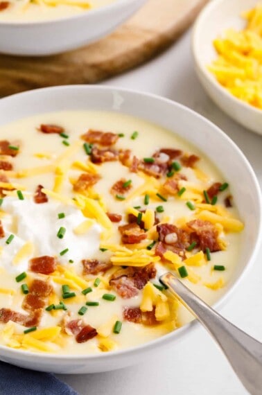 A bowl of creamy cheesy potato soup topped with cheese, sour cream, and bacon.