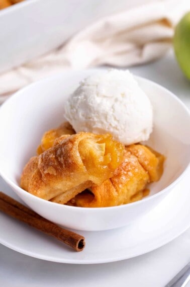 Apple dumplings in a white bowl topped with vanilla ice cream.