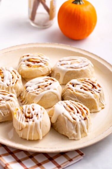 A plate of pumpkin cinnamon rolls topped with cream cheese frosting.