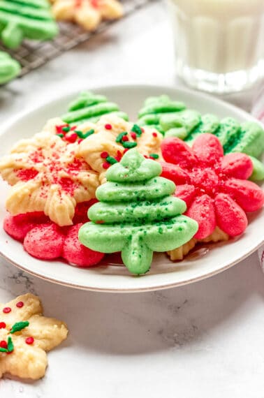 A plate of cream cheese spritz cookies in the shape of Christmas trees, flowers, and snowflakes.