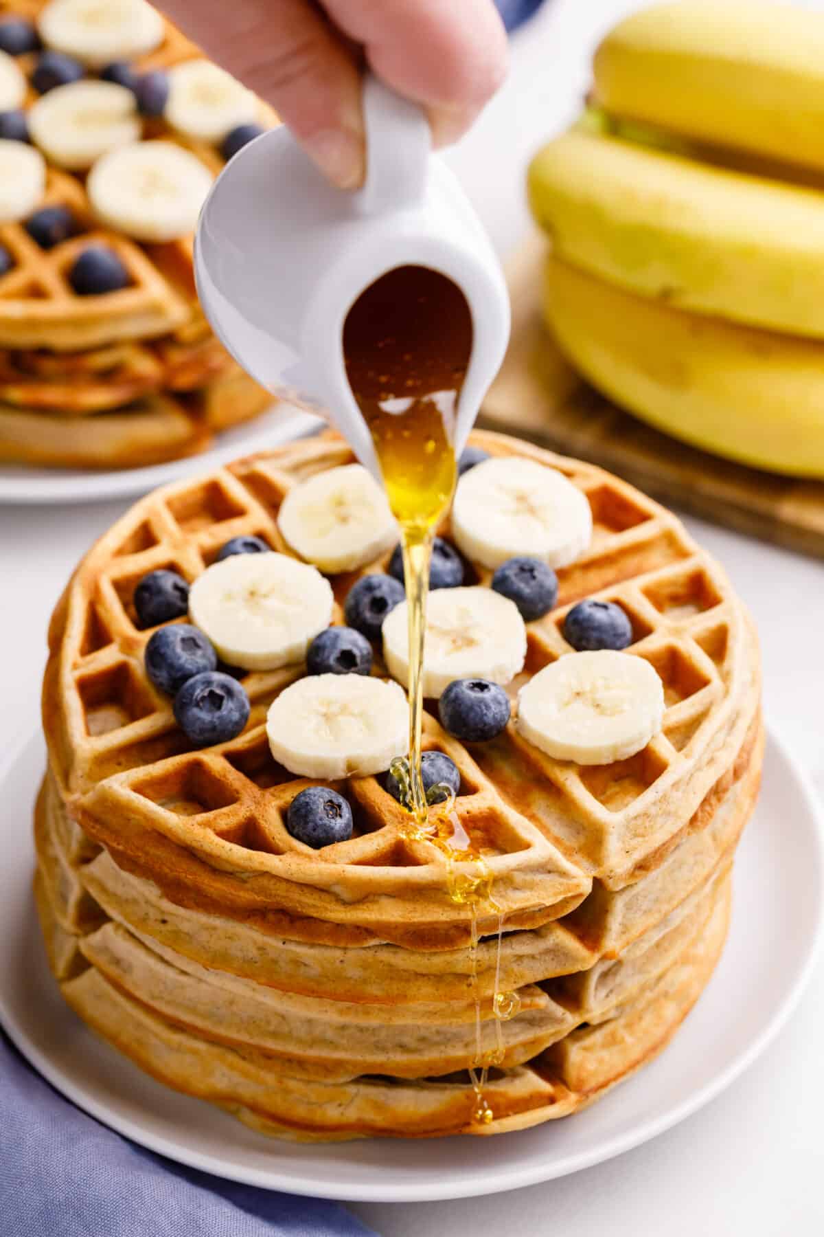 Pouring syrup onto stack of homemade banana waffles
