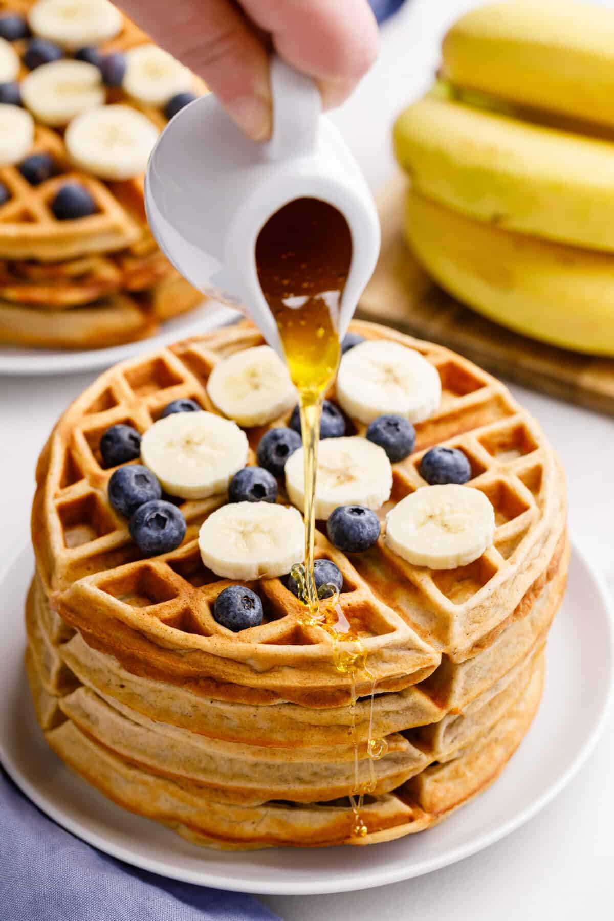 How to Make Waffles with Pancake Mix A stack of waffles with blueberries and bananas with syrup being poured on top.