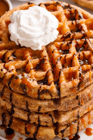 A stack of churro waffles topped with whipped cream and chocolate sauce.