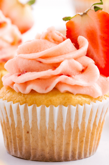 Strawberry lemon cupcakes with strawberry frosting and a halved strawberry.