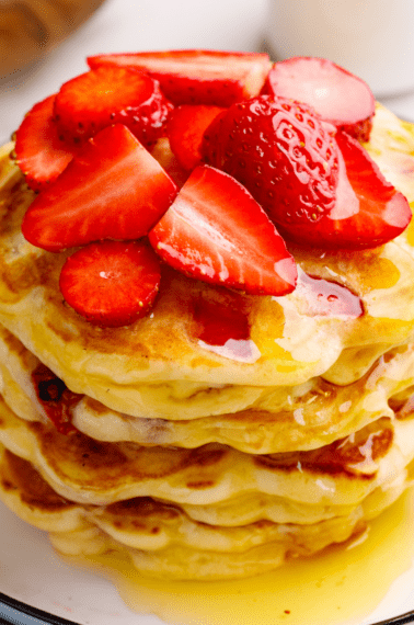A stack of strawberry pancakes topped with sliced strawberries.