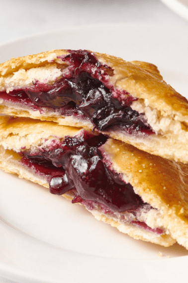 A blueberry hand pie split in half and stacked on a plate.