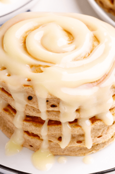 A stack of cinnamon pancakes with cream cheese glaze on a plate.