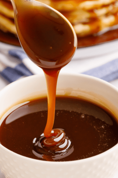 A bowl of homemade pancake syrup with a spoon lifting a scoop.