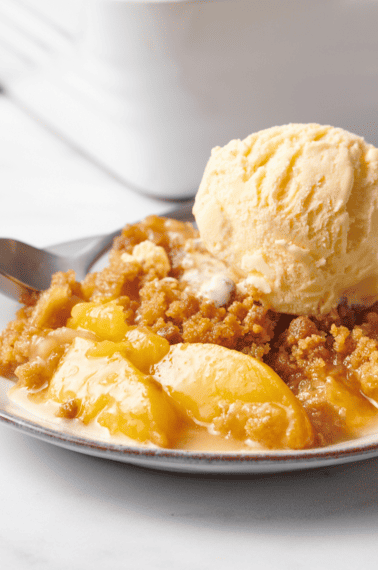 A plate of peach crumble topped with a scoop of vanilla ice cream.