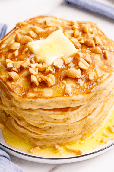 A stack of peanut butter pancakes topped with chopped peanuts and butter.