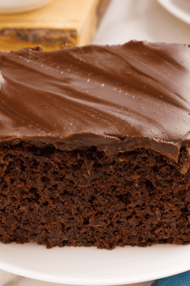A slice of chocolate zucchini cake topped with ganache on a plate.