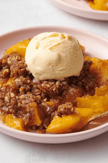 A plate of peach crisp topped with vanilla ice cream.