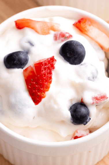 A spoon lifting a bite of red white and blue cheesecake salad from a bowl.