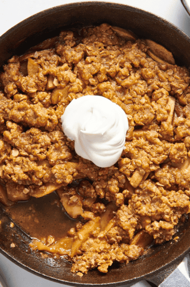 Overhead image of a skillet apple crisp topped with whipped cream.
