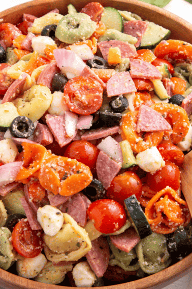 A bowl of tortellini pasta salad with a wooden spoon on the side.