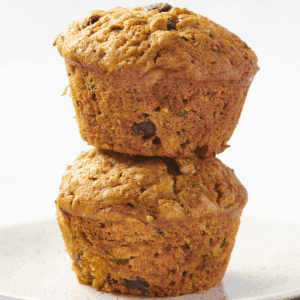 Two moist zucchini muffins with chocolate chips on top of each other.