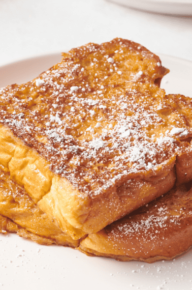 Two pieces of eggnog French toast topped with powdered sugar.