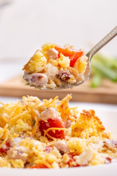 A spoon lifting a bite of Southern cornbread salad from a plate.