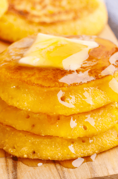 A stack of three cornbread fritters topped with butter and honey.