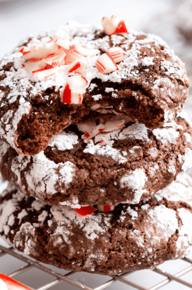 Three chocolate mint crinkle cookies stacked on top of each other with the top cookie missing a bite.