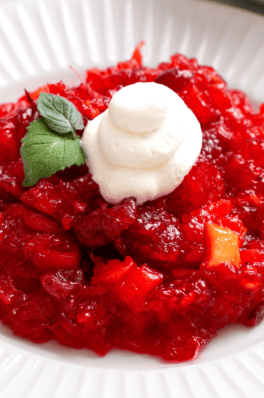 A bowl of cranberry jello salad topped with whipped cream.