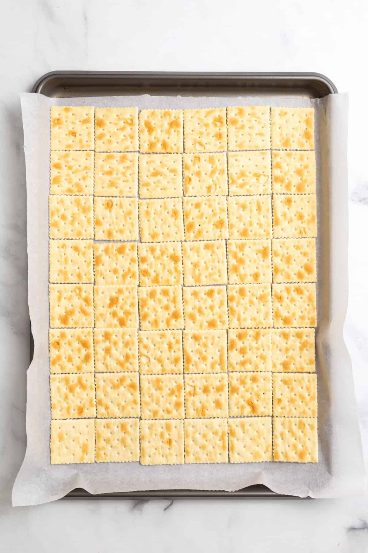parchment-lined baking sheet with saltines arranged at the bottom.
