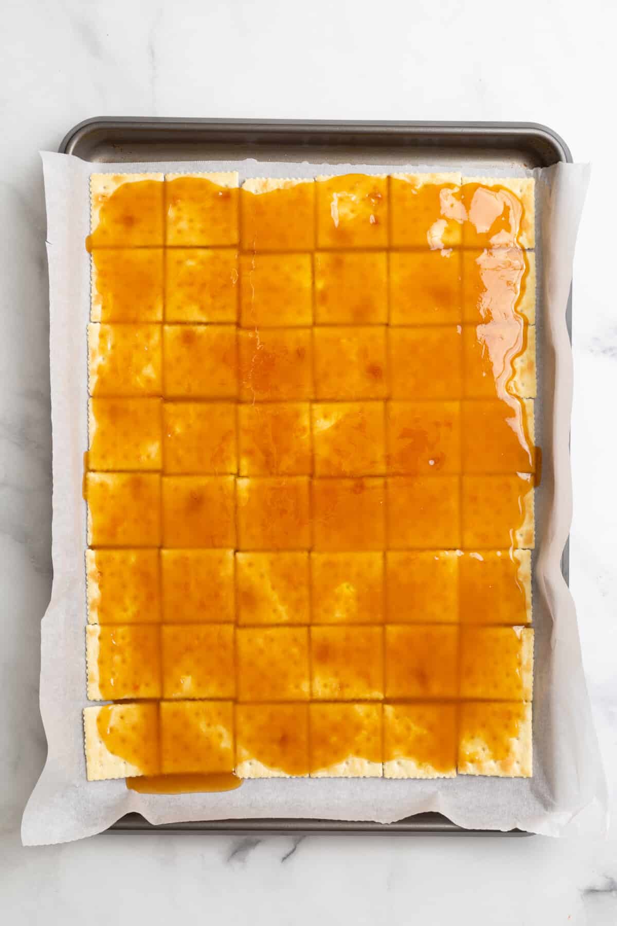 parchment-lined baking sheet with saltines arranged at the bottom and layered with caramel on top.