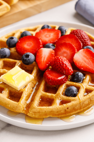 A buttermilk waffle topped with strawberries, blueberries, butter, and syrup.