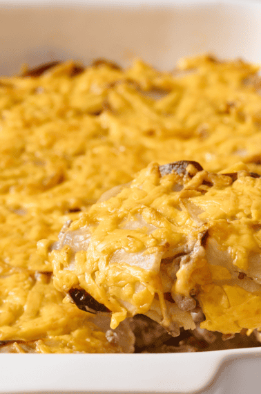 A spoon lifting a scoop of hamburger and potato casserole from a baking dish.