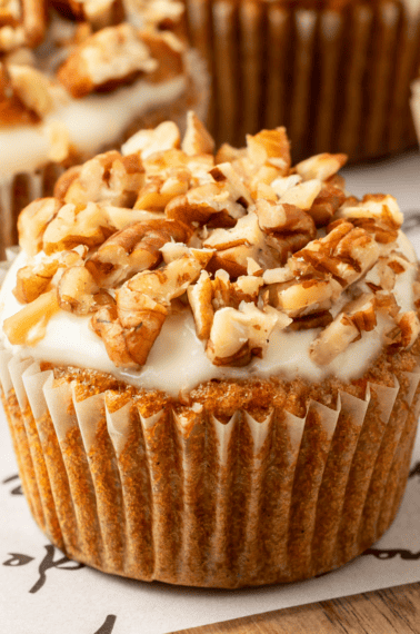 A carrot cake muffin with cream cheese glaze topped with pecans.