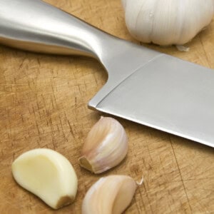 A knife next to garlic bulbs and three cloves of garlic.