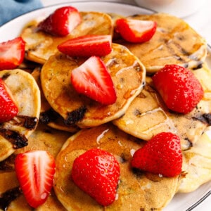 A plate of mini chocolate chip pancakes topped with strawberries and syrup.
