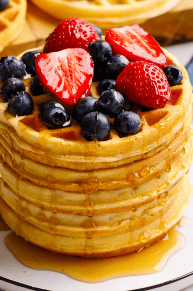 A stack of mini waffles topped with berries and syrup.