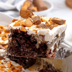 A slice of Butterfinger poke cake being lifted from a pan.