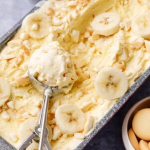 An ice cream scoop holding a scoop of banana pudding ice cream on top of a loaf pan.