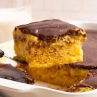 A slice of Boston Cream Poke Cake being lifted from a pan.