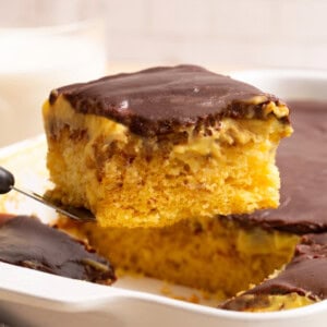 A slice of Boston Cream Poke Cake being lifted from a pan.