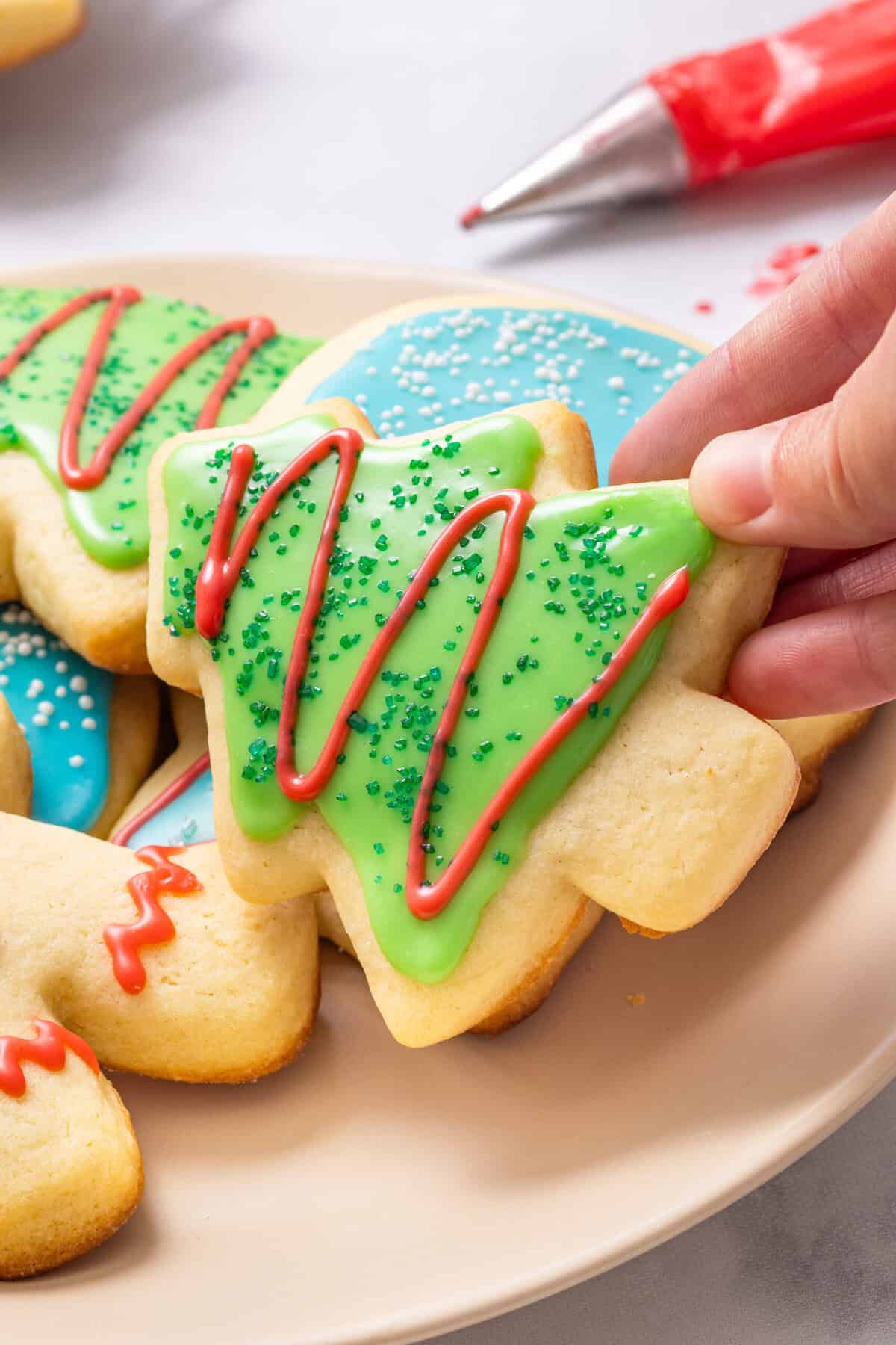Sugar Cookie Icing A hand grabbing a cut out Christmas tree cookie covered in sugar cookie icing.