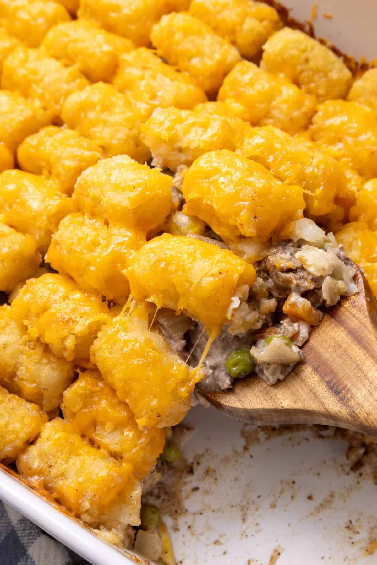 Tater Tot Casserole A close up of Tater Tot Casserole being scooped up with a wooden spoon.