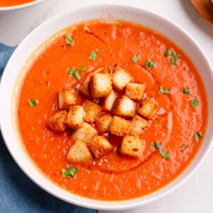 tomato soup in a white bowl with croutons, basil and cream