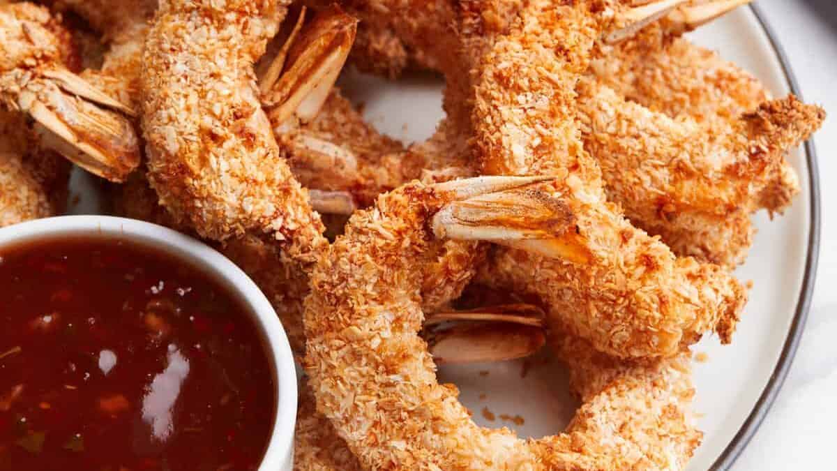 A plate of air fryer coconut shrimp with a side of chili sauce.
