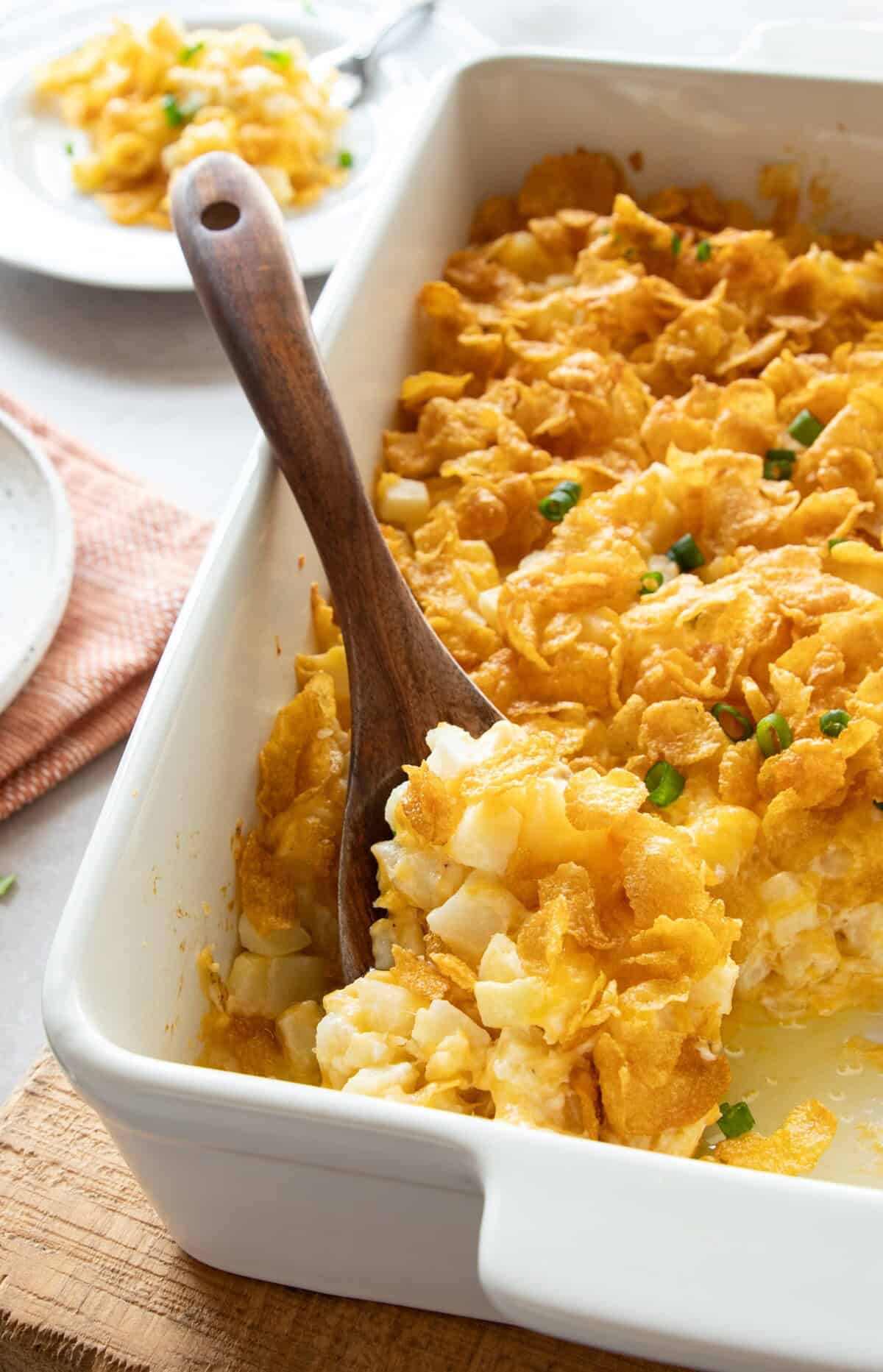 Overhead view of cheesy potatoes in casserole dish being scooped with wooden spoon