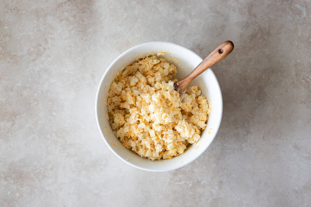Overhead view of cheesy potato mixture in bowl with wooden spoon